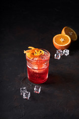 Negroni Cocktail with Orange Twist and Pin, on Dark Background, , and next to it orange and ice. Beverage Photography.
