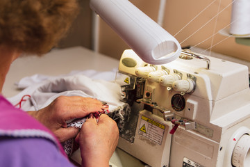 an elderly woman sews on a sewing machine. tailor embroiders in production.