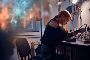 Talanted young woman is working on her own project at glass workshop.