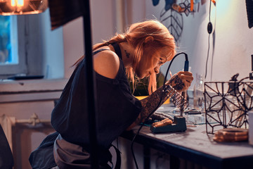 Beautiful diligent woman is doing soldering at her own artisan lamp studio. - obrazy, fototapety, plakaty