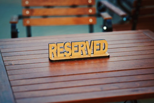 Wooden reserved sign on summer terrace of the restaurant. Reservation sign on the table in restaurant. Top view of reserved sign on wooden table. Handmade wooden sign RESERVED, table setting element