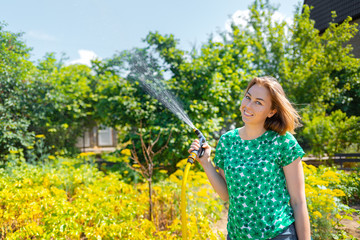 A young blonde woman spraying plants in his garden. The concept of a summer hobby and gardening. Close up