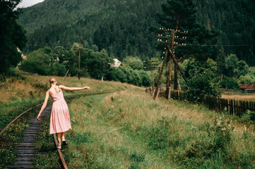 Young girl walking on the railway. Woman in pink dress walking on railroad tracks.