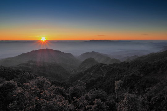 Mountain view misty morning of top hills around with sea of fog with red and yellow sun light in the sky background, sunrise at Doi Ang Khang, Monzone view point, Chiang Mai, Thailand.