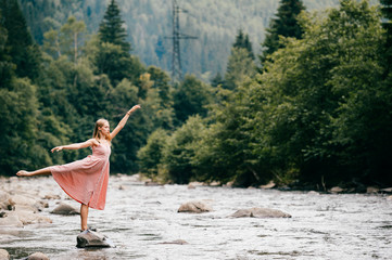 Young graceful ballerina girl balancing on stone in the river.