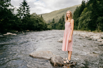 Caucasian young girl posing at stone in the river in summer day.