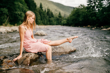 Young happy girl kicking foot in river and splashing water.