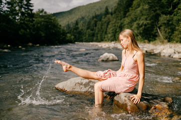 Young happy girl kicking foot in river and splashing water.