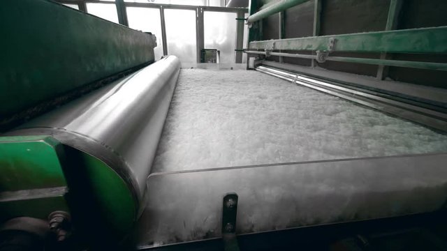 Plant machine rolls white polyester material, moving on a line.