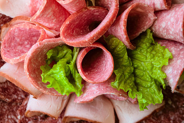 Sliced ham and raw smoked sausage rolls with lettuce leaves