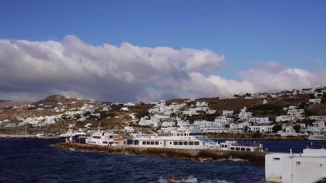 Mykonos, Greece moored ships against Greek island landscape background. Delos Island tourist ships with background of whitewashed low rise traditional Mykonean houses at Mykonos Town (Chora).