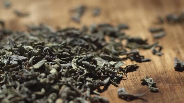 SLOW MOTION: Tea leaves fall on a pile of a green tea - Macro shot. Beautiful view.