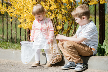A cute blonde with blue eyes is playing with a teddy bear and a hoop to catch butterflies. spring...