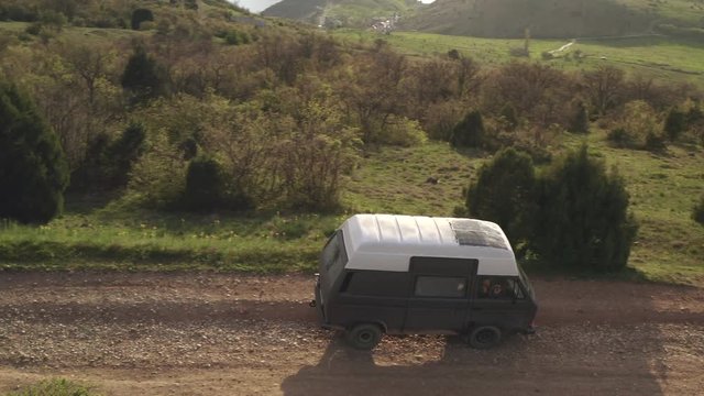 Flying over gray van t3 car gently down hill on wooded area. Drive on old mountain gravel road. Mountain landscape view. Travel destinations. Journey road. Aerial view