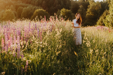 A girl walks through a beautiful blooming field at sunset