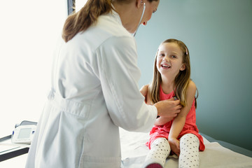 Woman doctor holds stethoscope to young girl's chest