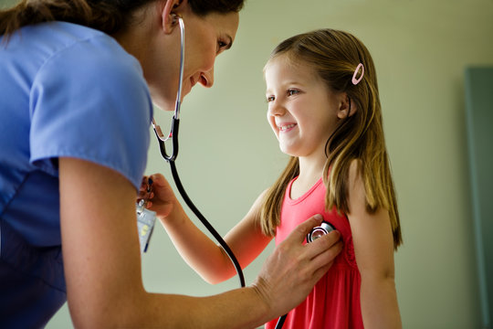 Woman doctor holds stethoscope to young girl's chest
