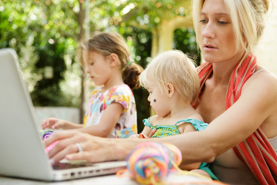Mother works on laptop with baby on her lap