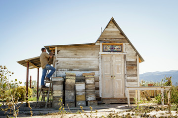 Man hammering roof of small rustic wooden building