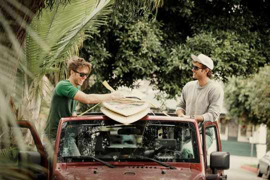 Young Men Fasten Surfboards To Car Roof