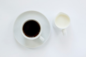 Cup of espresso coffee with saucer and a small pitcher of milk on white background. Top view. Close up image.