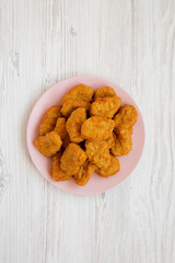 Chicken nuggets on a pink plate on a white wooden surface, top view. Overhead, from above, flat lay.