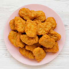 Top view, chicken nuggets on a pink plate on a white wooden background. Overhead, from above, flat lay. Closeup.