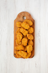 Chicken nuggets on a rustic wooden board on a white wooden background, top view. Flat lay, from above, overhead.