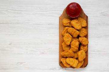 Chicken nuggets with ketchup on a rustic wooden board on a white wooden background, top view. Flat lay, from above, overhead. Copy space.