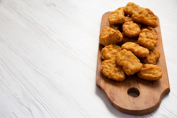 Chicken nuggets on a rustic wooden board on a white wooden background, low angle view. Copy space.
