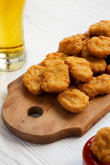 Chicken nuggets with ketchup and glass of cold beer on a white wooden surface, low angle view. Close-up.