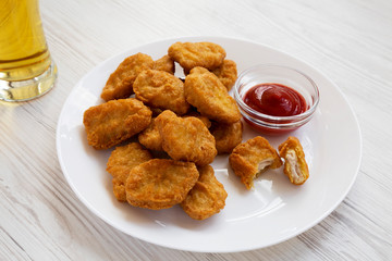 Side view, chicken nuggets with ketchup and glass of cold beer on a white wooden background. Close-up.