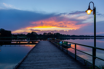 Zachód słońca nad jeziorem Kalwa w Polsce. Odbicie nieba w wodzie, pomost.