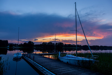 Zachód słońca nad jeziorem Kalwa w Polsce. Odbicie nieba w wodzie, łodzie żaglowe przy...