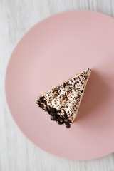 A piece of tiramisu cake on a pink plate on a white wooden background, top view. Close-up.