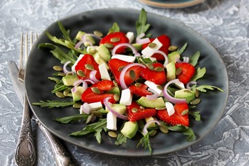salad with strawberries and avocado, arugula, feta cheese, pumpkin seeds, red onion