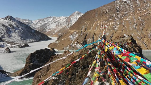 Drone flight over prayer flags reveals beautiful Winter landscape of snow covered mountains and frozen lakes at high altitude plateau in Tibet