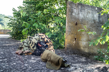 Young sniper soldier special force covered with camouflage net aiming to the enemy waiting for the...
