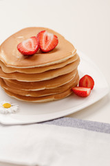 Homemade breakfast. American style pancakes served with fresh strawberry  on white table and towel.