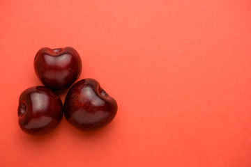 Close up of three cherries in the left part of the coral background.