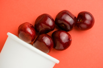 Close up of pile raw cherries above paper cup on the diagonal coral background.