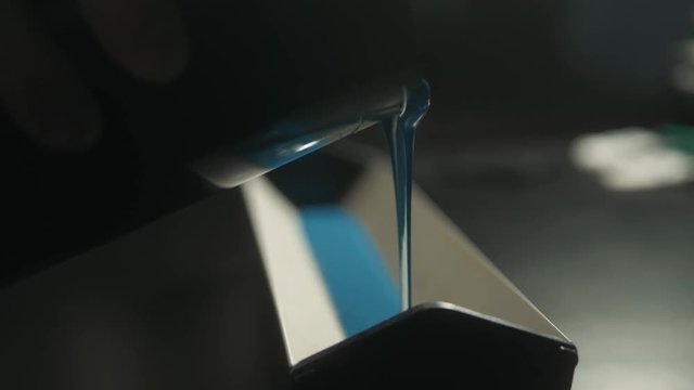 Young caucasian man pouring container with blue color in workshop in industrial print studio. Craftsman print on t shirt silkscreen.