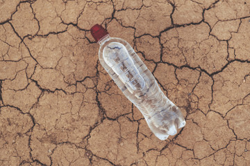 A bottle of water on the dried ground. The concept of thirst, dehydration.