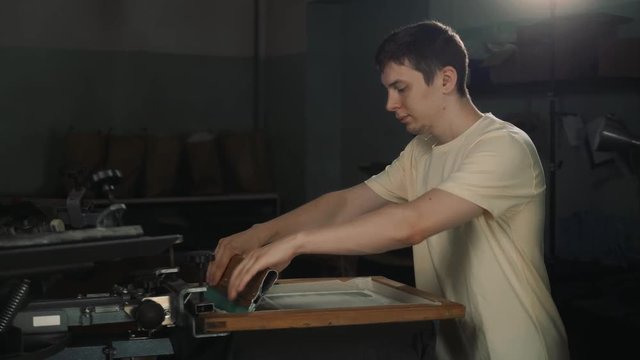 Close up timelapse of male hands exploring traditional silkscreen print, creating an image fabric clothing by pressing ink through a screen