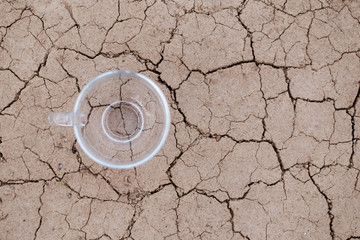 Empty glass cup on the dried ground. The concept of thirst, dehydration, water needs.
