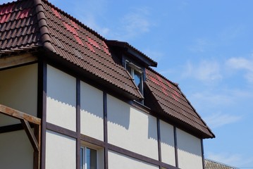 part of a private house with a brown tiled roof and a window against the blue sky