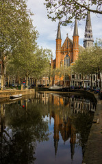 Gouda, Holland, Netherlands, April 23, 2019, Gouwekerk church near a bridge on a canal in Gouda old town. Flowers in a flowerbeds, boat on the water.