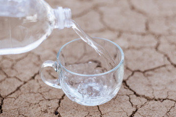 Pour water into a cup on dry ground. The concept of thirst, dehydration, lack of water.