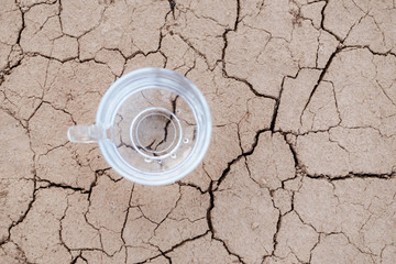 Concept of thirst, dehydration, lack of water. A cup of water on cracked dry ground.