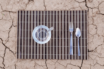Water is the most necessary food for a person. A cup of water and cutlery on the dried ground.